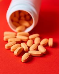 Image showing Pills spilling out of pill bottle on red. Top view with copy space. 