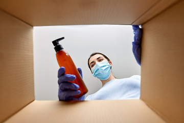 Image showing woman in mask unpacking parcel box with cosmetics