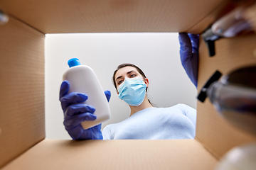 Image showing woman in mask unpacking parcel box with cosmetics