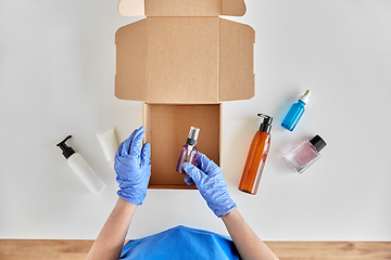 Image showing hands in gloves packing parcel box with cosmetics