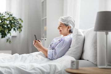 Image showing happy senior woman using smartphone in bed at home