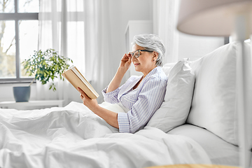 Image showing old woman in glasses reading book in bed at home