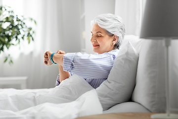 Image showing happy old woman with health tracker sitting in bed