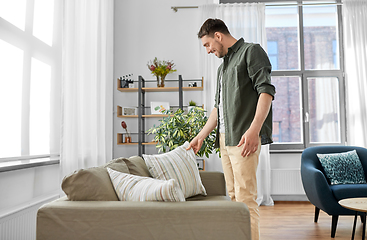 Image showing happy smiling man arranging sofa cushions at home