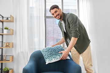 Image showing happy smiling man arranging chair cushion at home