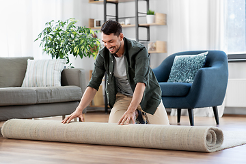 Image showing happy smiling young man unfolding carpet at home