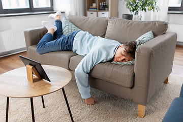 Image showing bored man with tablet pc lying on sofa at home