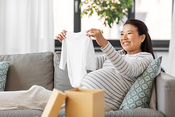 Image showing happy pregnant woman with baby's bodysuit at home