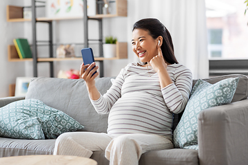 Image showing pregnant woman with phone and earphones at home