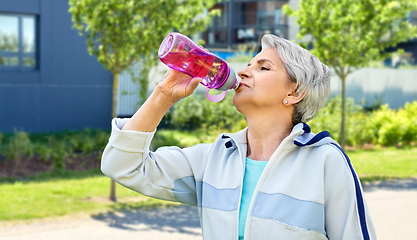 Image showing old woman drinking water after exercising in city