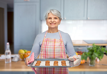 Image showing senior woman in apron with cookies on baking pan