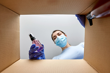 Image showing woman in mask unpacking parcel box with cosmetics