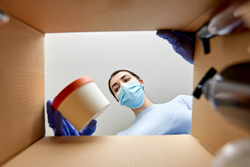 Image showing woman in mask unpacking parcel box with cosmetics