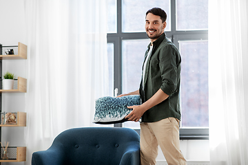 Image showing happy smiling man arranging chair cushion at home