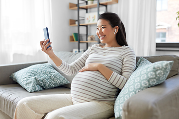 Image showing pregnant woman with phone and earphones at home