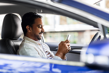 Image showing smiling indian man in car using smartphone