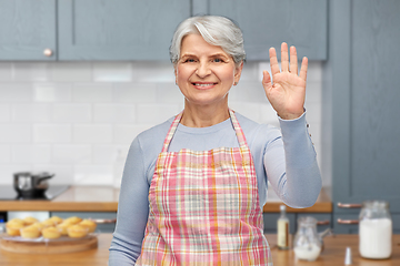 Image showing smiling senior woman in apron waving hand