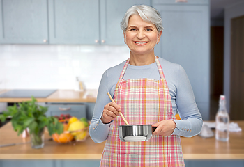 Image showing senior woman in apron with pot cooking food