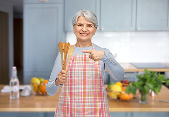 Image showing smiling senior woman in apron with wooden spoons