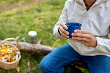 Image showing man with basket of mushrooms drinks tea in forest