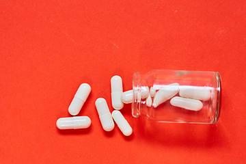 Image showing Pills spilling out of pill bottle on red. Top view with copy space. 