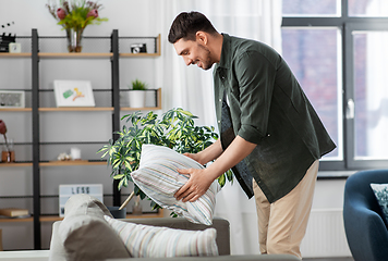 Image showing happy smiling man arranging sofa cushions at home