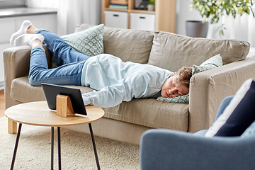 Image showing bored man with tablet pc lying on sofa at home