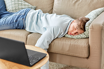 Image showing bored man with laptop lying on sofa at home