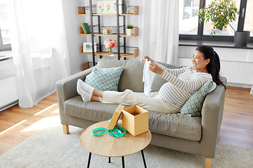 Image showing happy pregnant woman with baby's bodysuit at home