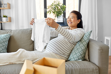 Image showing happy pregnant woman with baby's bodysuit at home