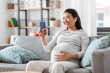 Image showing pregnant woman with phone and earphones at home