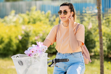 Image showing happy woman with earphones riding bicycle in city