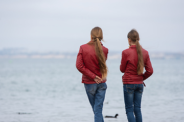 Image showing Two girls in identical clothes look at the sea, close-up, view from the back