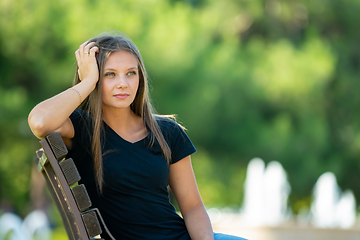 Image showing A girl sits on a bench propping her head up with her hand, close-up