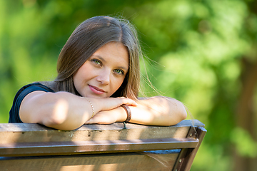 Image showing Portrait of a beautiful girl sitting on a bench and looking happily into the frame