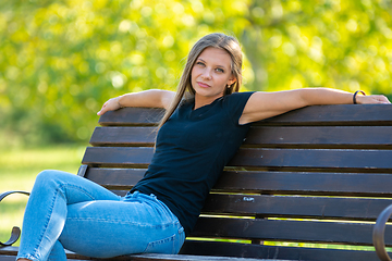 Image showing A girl sits on a bench in a sunny park and looks into the frame