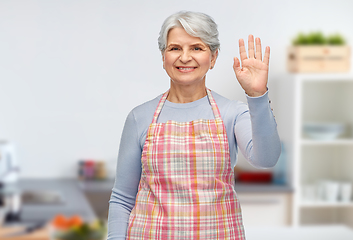 Image showing smiling senior woman in kitchen apron waving hand