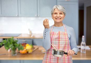 Image showing senior woman in apron with pot cooking food