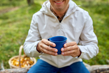 Image showing man with basket of mushrooms drinks tea in forest