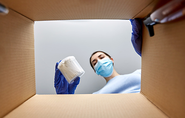 Image showing woman in mask unpacking parcel box with cosmetics