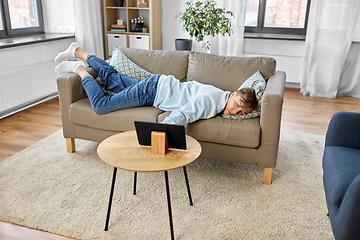 Image showing bored man with tablet pc lying on sofa at home