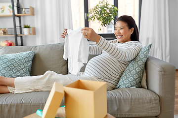 Image showing happy pregnant woman with baby's bodysuit at home