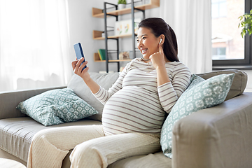 Image showing pregnant woman with phone and earphones at home