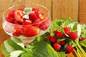 Image showing strawberries in transparent bowl and bunches with leaves