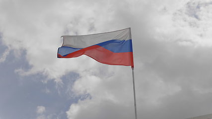 Image showing Russian flag on the flagpole waving in the wind against a blue sky with clouds. Slow motion