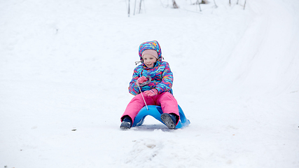 Image showing Cheerful girl riding a sled downhill on a snow covered sledge trail in a white sunny winter mountain landscape