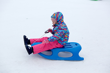 Image showing Cheerful girl riding a sled downhill on a snow covered sledge trail in a white sunny winter mountain landscape