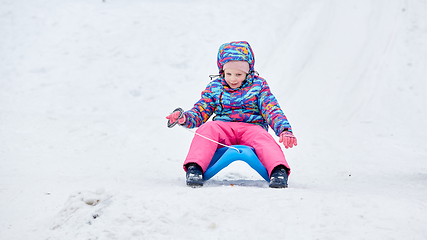 Image showing Cheerful girl riding a sled downhill on a snow covered sledge trail in a white sunny winter mountain landscape