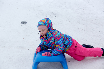 Image showing Cheerful girl riding a sled downhill on a snow covered sledge trail in a white sunny winter mountain landscape