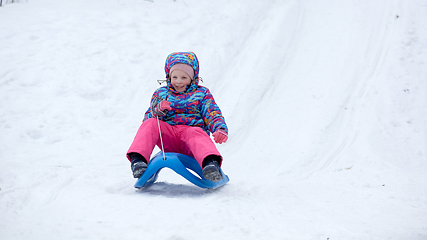 Image showing Cheerful girl riding a sled downhill on a snow covered sledge trail in a white sunny winter mountain landscape